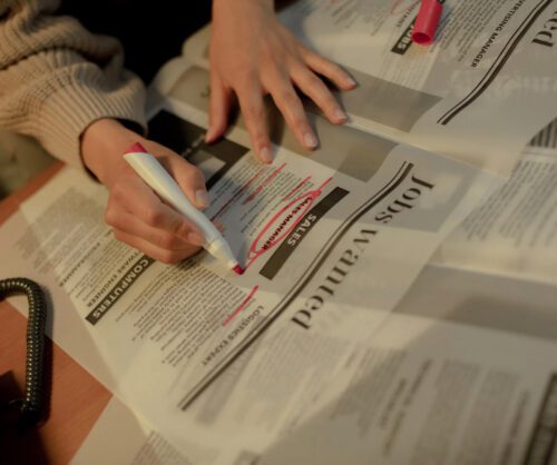 Persona subrayando con rotulador anuncios de empleo en un periódico, destacando ofertas de trabajo en la sección de vacantes.